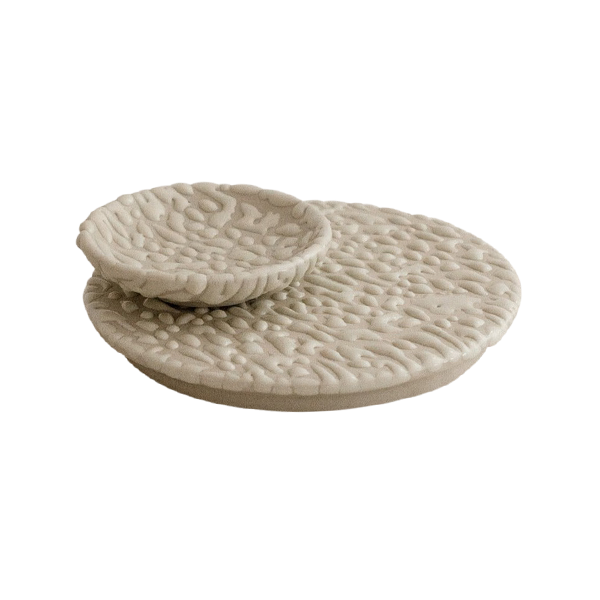 A ceramic vanity set consisting of a round plate and a round dish with a textured beige surface.